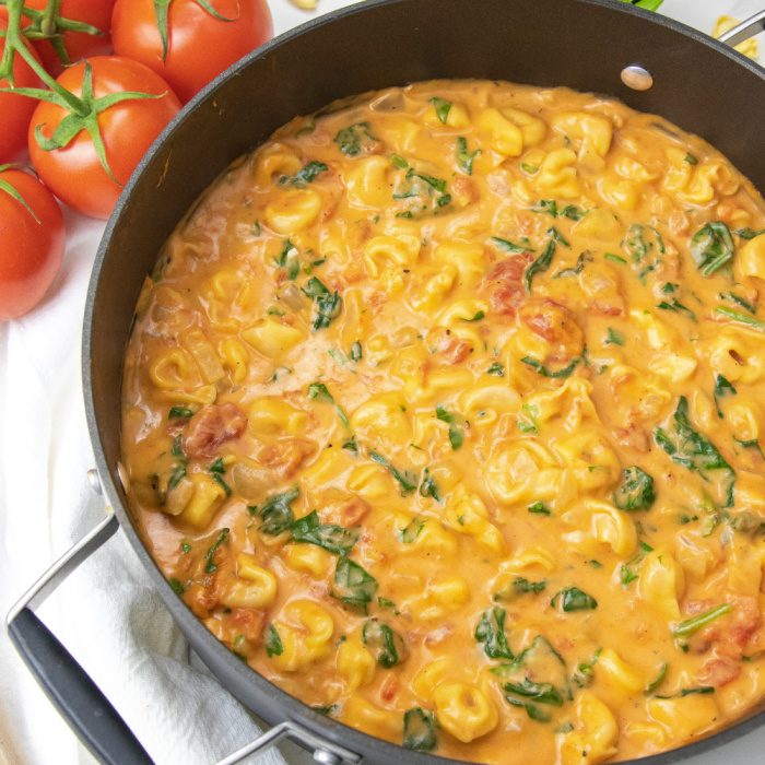 spinach tortellini soup in pot with tomatoes behind it 