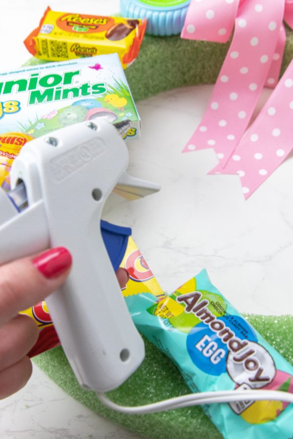 Easter Wreath Gift Idea that is great for teachers, neighbors and more. A fun alternative to an Easter basket you have to try this year. #passion4savings #easter #diy #wreath #giftidea #alternative #easterbasket #teacher #spouse #teen #neighbor holding hot glue gun above Easter wreath