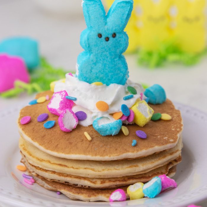Easter peeps pancakes are a fluffy pancake filled with bits of peeps. This is a marshmallow pancake perfect for Easter morning breakfast. #passion4savings #easter #pancakes #peeps #tradition #spring #morning #eastermorning stack of pancakes with whipped cream and peep on top