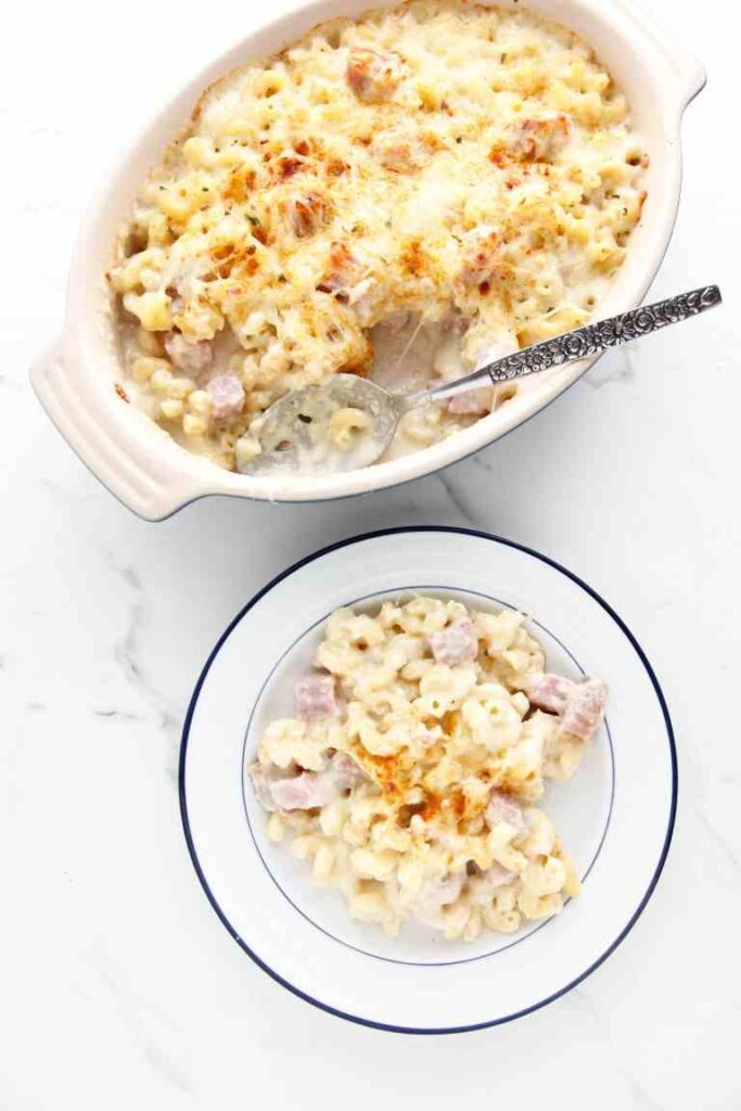 ham and macaroni and cheese on a plate with casserole dish behind it 