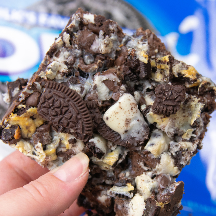 Oreo Magic Bars take minutes to make, and are delicious sweet magic bars. Loaded with cookies and cream bars, Oreos, chocolate chips and more. Give this easy Oreo cookie recipe a try today. #passion4savings #oreo #cookiesandcream #easy #quick #partyfood #dessert holding oreo cookie bar