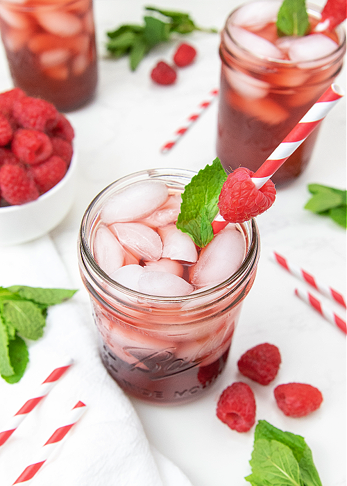 drink in mason jar garnished by mint leaves and raspberries