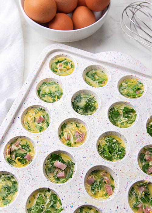 mini muffin tins filled with egg, spinach, ham, and cheese