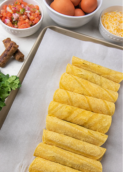 rolled up taquitos on a baking sheet