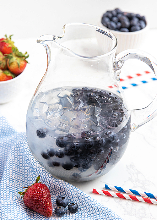 Patriotic Party Punch is an easy and FESTIVE beverage for your 4th of July cookout! Even though it's clear, it packs BIG flavor!! patriotic party punch step by step image with part of the punch and blueberries in a clear glass pitcher