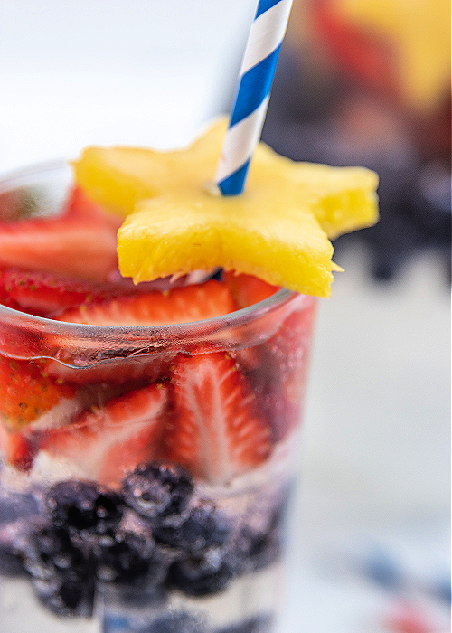 Patriotic Party Punch is an easy and FESTIVE beverage for your 4th of July cookout! Even though it's clear, it packs BIG flavor!! patriotic party punch with strawberries and blueberries and a blue straw
