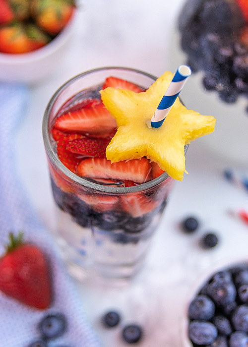 Patriotic Party Punch is an easy and FESTIVE beverage for your 4th of July cookout! Even though it's clear, it packs BIG flavor!! a glass of patriotic party punch garnished with fruit