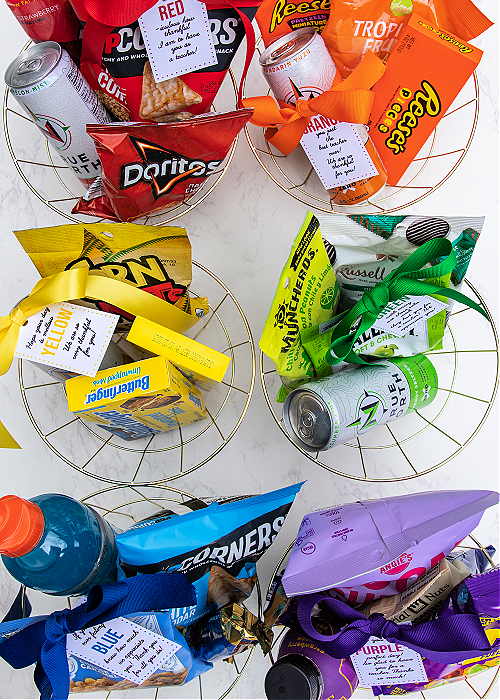 teacher appreciation gift baskets in red orange yellow green blue and purple with snacks of each color inside the baskets tied with free printable gift tags