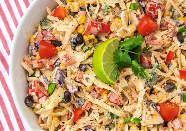 mexican coleslaw in a white serving bowl garnished with a slice of lime and a sprig of cilantro