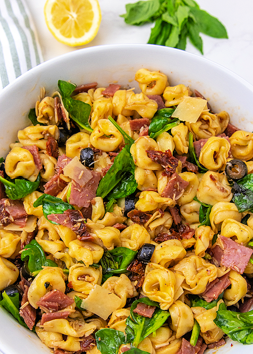 Tuscan Tortellini Salad combines baby spinach, tortellini, salami, black olives, sun-dried tomatoes and more- a light, delicious summer meal! tuscan tortellini salad mixed with balsamic vinaigrette dressing in a serving bowl