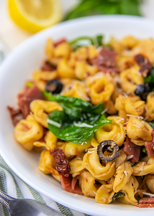 Tuscan Tortellini Salad combines baby spinach, tortellini, salami, black olives, sun-dried tomatoes and more- a light, delicious summer meal! tuscan tortellini salad in a white pasta bowl