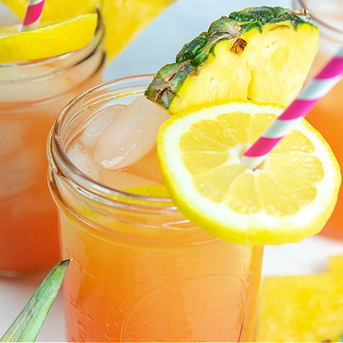 pineapple pink lemonade in a mason jar garnished with a wedge of pineapple and a lemon slice