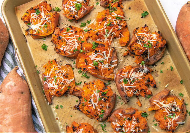 garlic parmesan smashed sweet potatoes on a cookie sheet sprinkled with parsley
