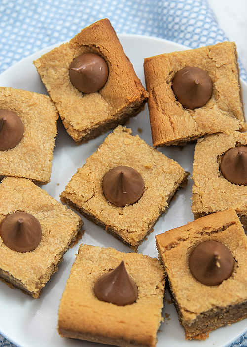 peanut butter blossom bars on a white serving plate with a blue towel in the background