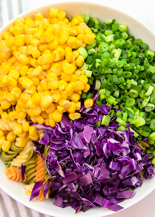 mardi gras pasta salad ingredients before mixing in a white mixing bowl