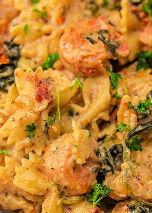 Creamy Garlic Butter Tuscan Shrimp Pasta is a delicious one-pan meal that is healthy, too! Sun-dried tomatoes, parmesan, garlic, and herbs combine for impeccable flavor! a closeup of creamy garlic butter Tuscan shrimp pasta with spinach and sun-dried tomatoes