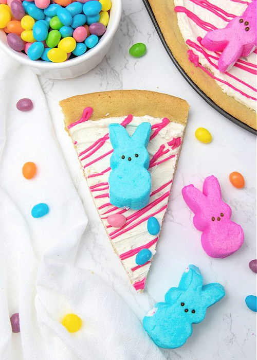 Over 20+ Easter Dessert Recipes that are CUTE and EASY to make for all your holiday occasions! Perfect for egg hunts, Easter dinner, and more. a slice of peeps dessert pizza topped with a blue peep