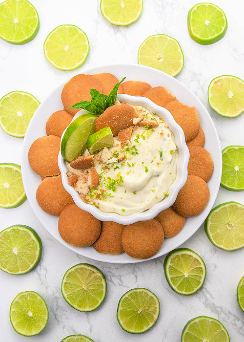 key lime pie dip in a white serving bowl surrounded by nilla wafers and slices of lime