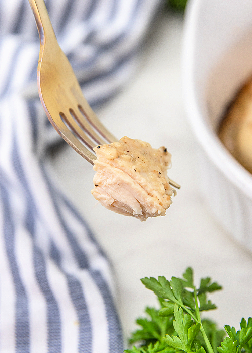 a bite of baked caesar chicken on a gold fork with a blue and white striped napkin in the background