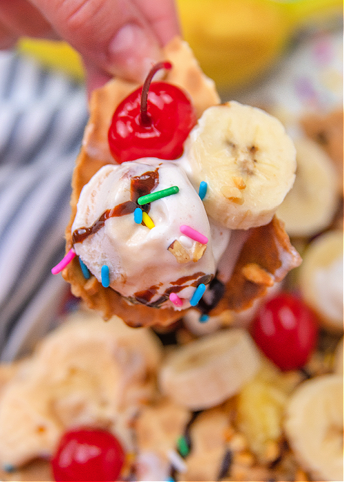 someone holding a banana split nacho made from a waffle cone and ice cream and toppings