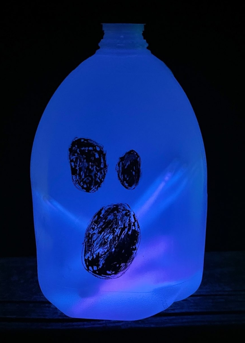 glow in the dark milk jug lantern made from blue glow sticks with a ghost face drawn on it